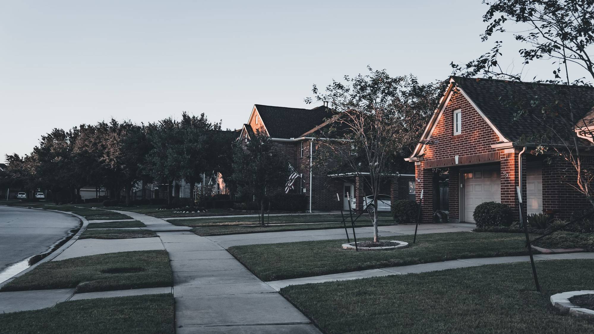 Brick houses with lawns and a curving sidewalk on a quiet suburban street