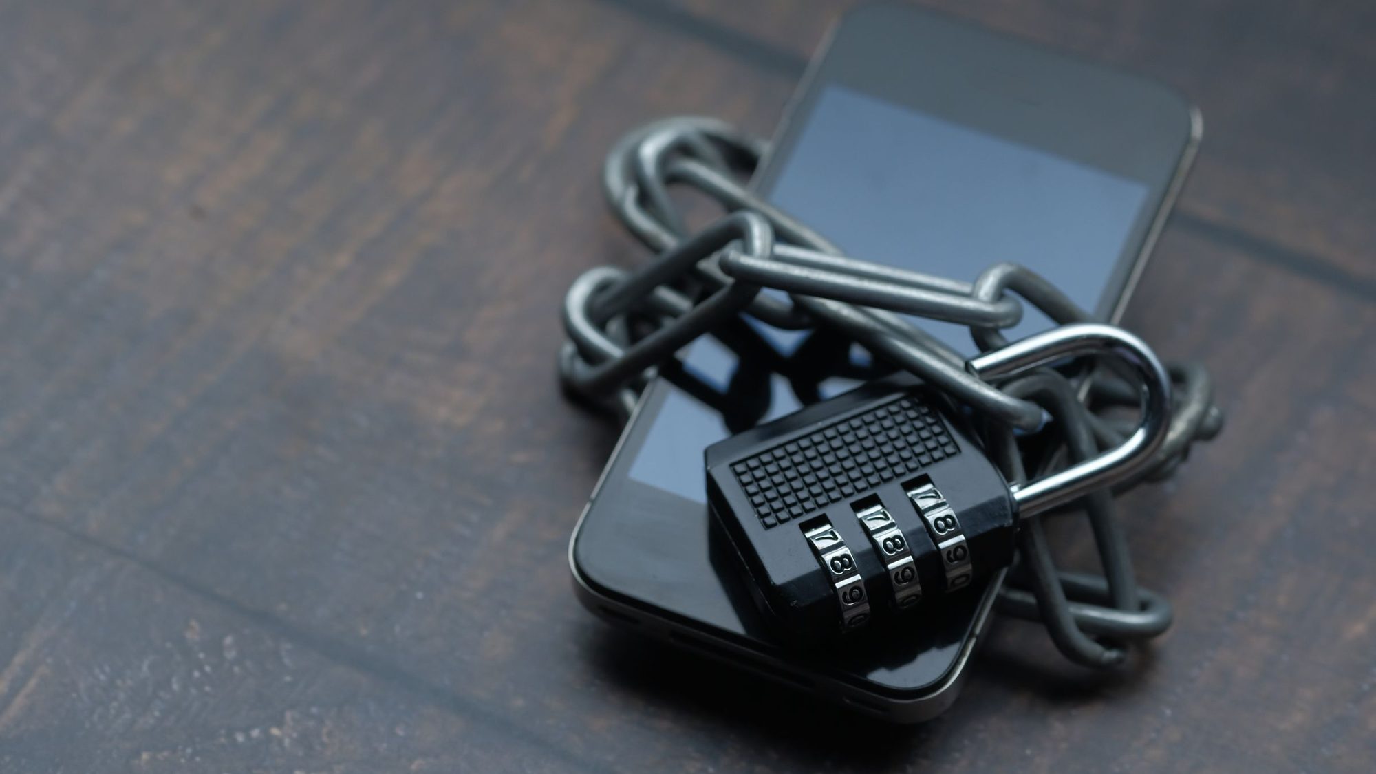 A smartphone wrapped in a metal chain with a combination padlock
