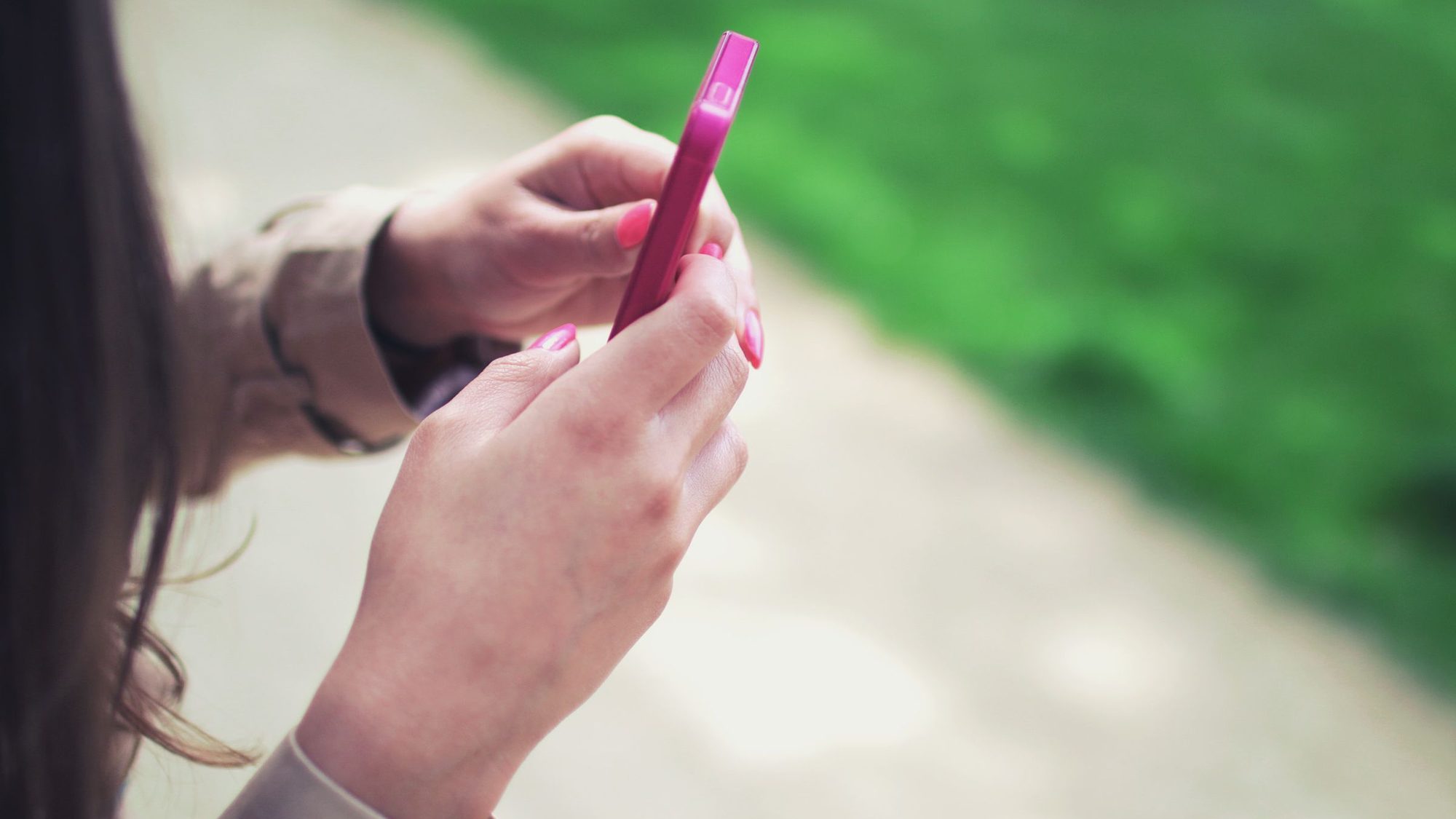 A woman types on a pink smartphone with both hands