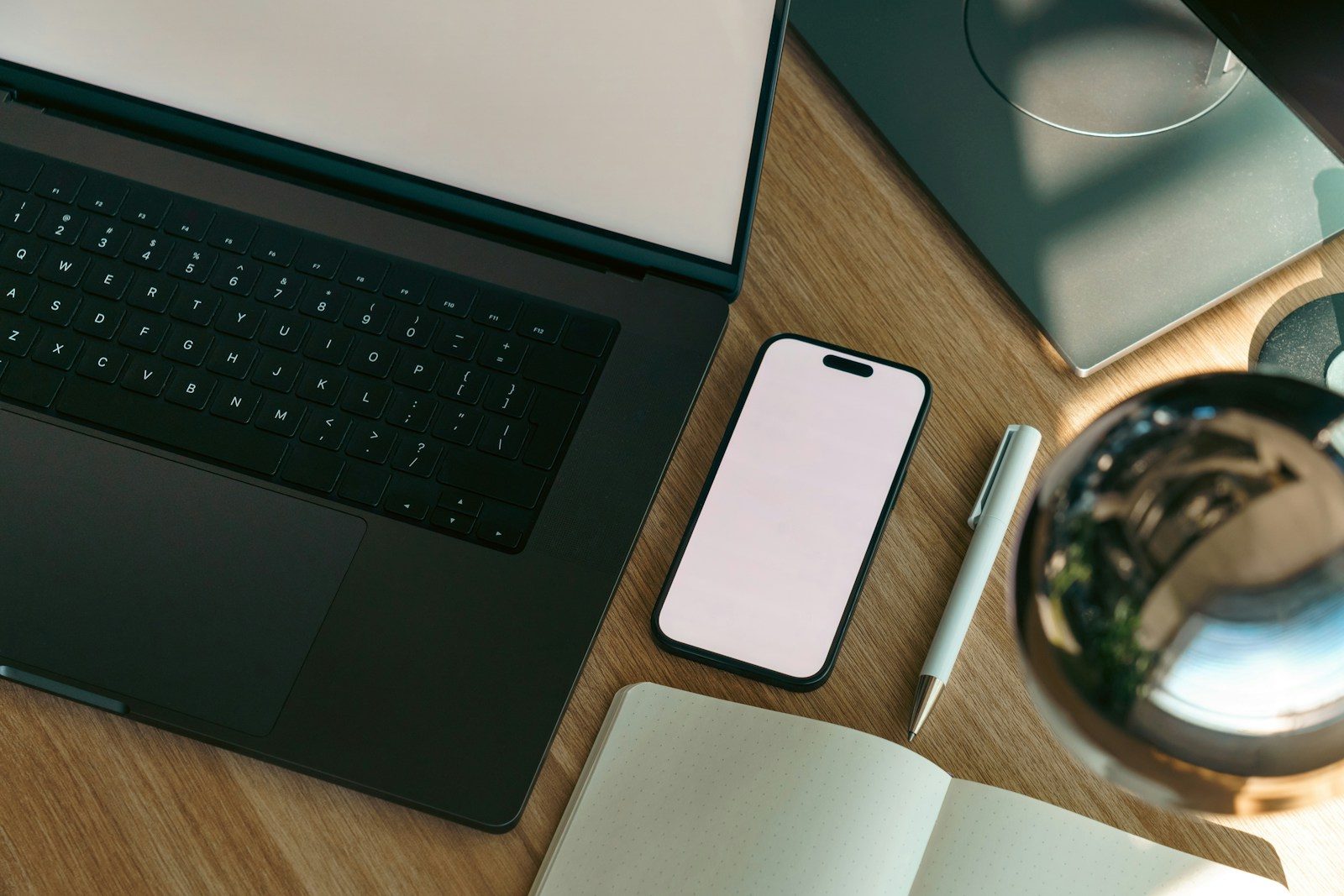 Laptop, smartphone, and notebook on a wooden desk, running SMS marketing and email marketing programs side by side from one workspace