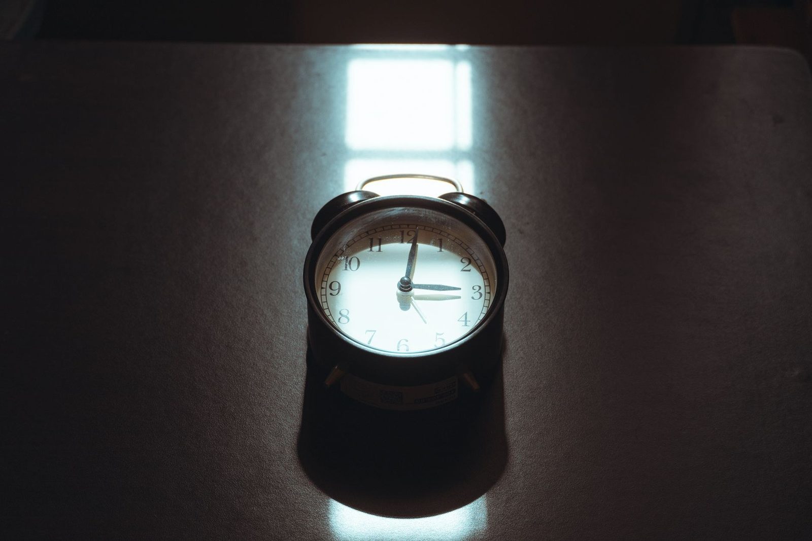A vintage alarm clock casting a long shadow across a desk in low light, the recipient's local clock that quiet hours are enforced against